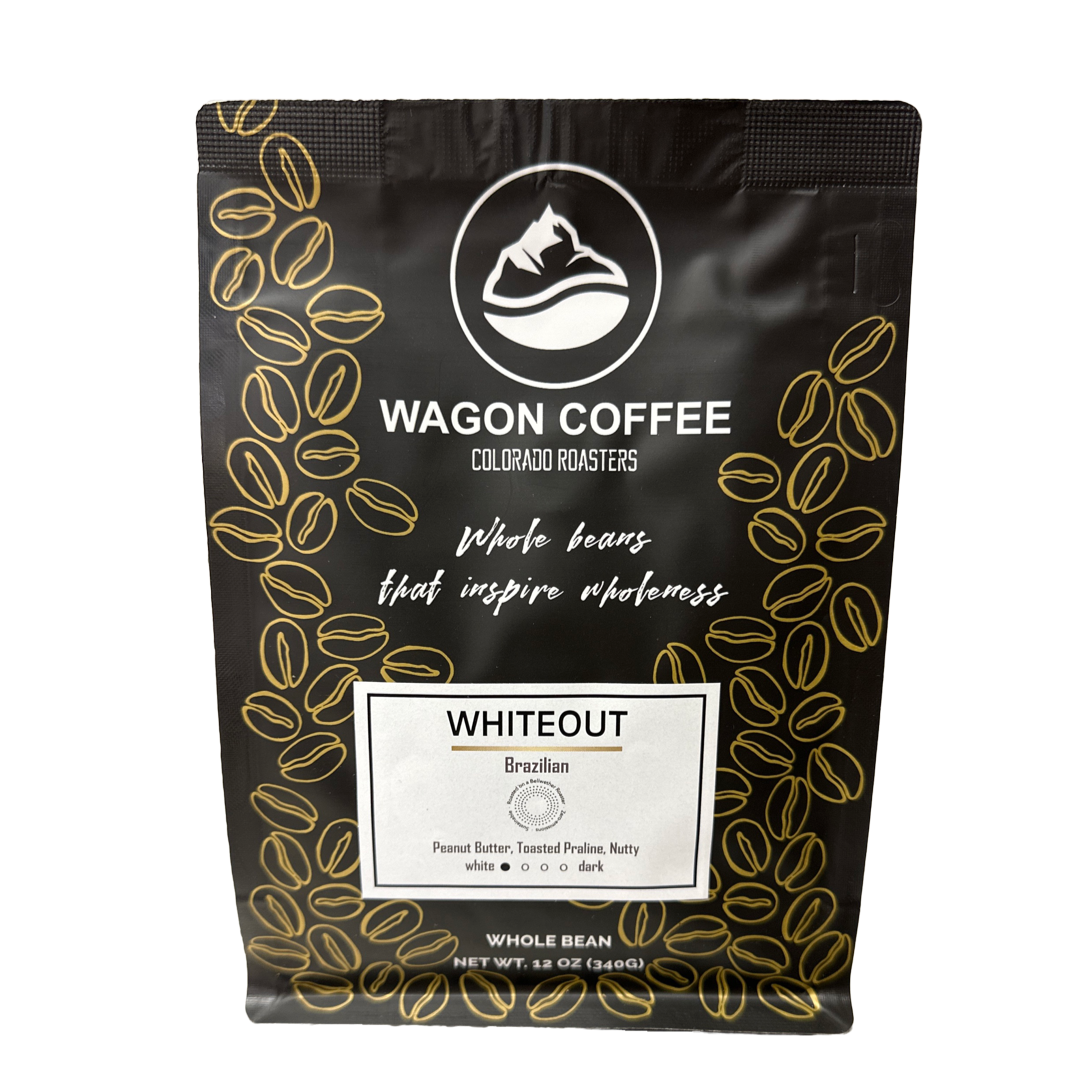 Whiteout 12:10 White Coffee by Wagon Coffee in a white cup with coffee beans and a spoon on a white surface.