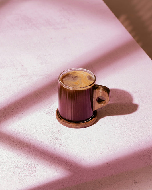 Glass mug with coffee on wooden coaster.