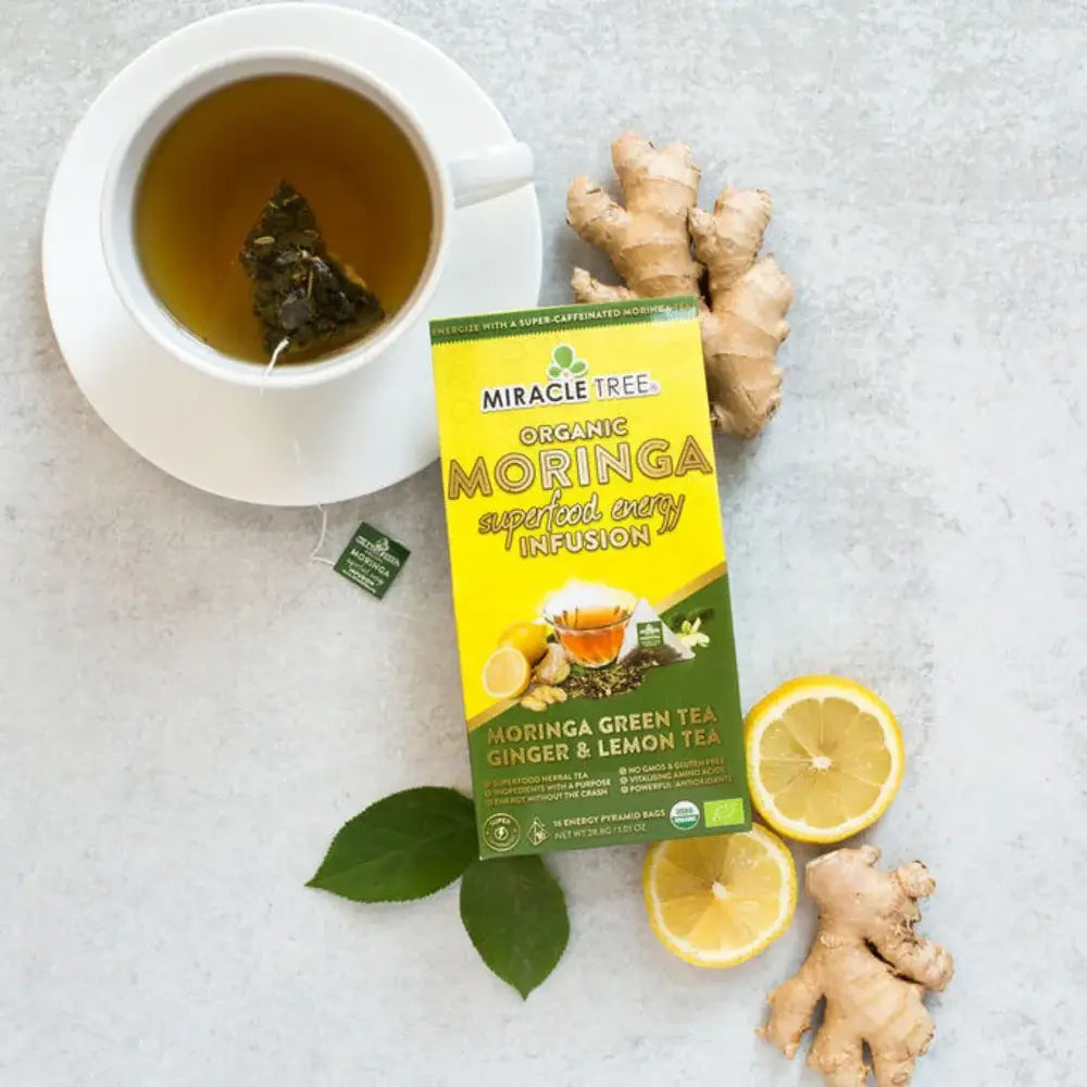 Organic Moringa Energy Tea by Miracle Tree with ginger and lemon, featuring vibrant tea leaves and fresh ginger root on a wooden surface.