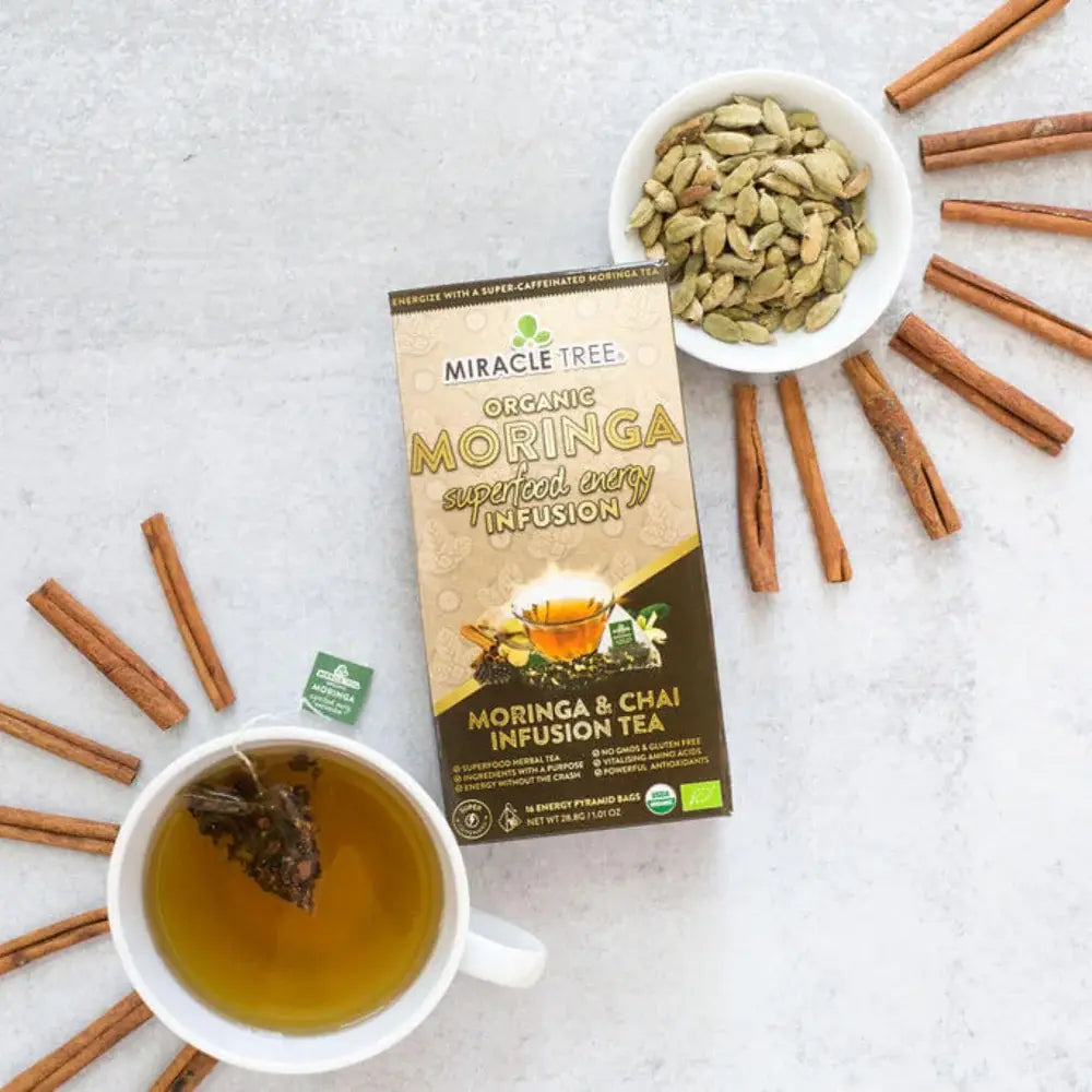 Organic Moringa Energy Tea by Miracle Tree with chai spice flavor, showcasing a steaming cup of herbal tea on a wooden table.