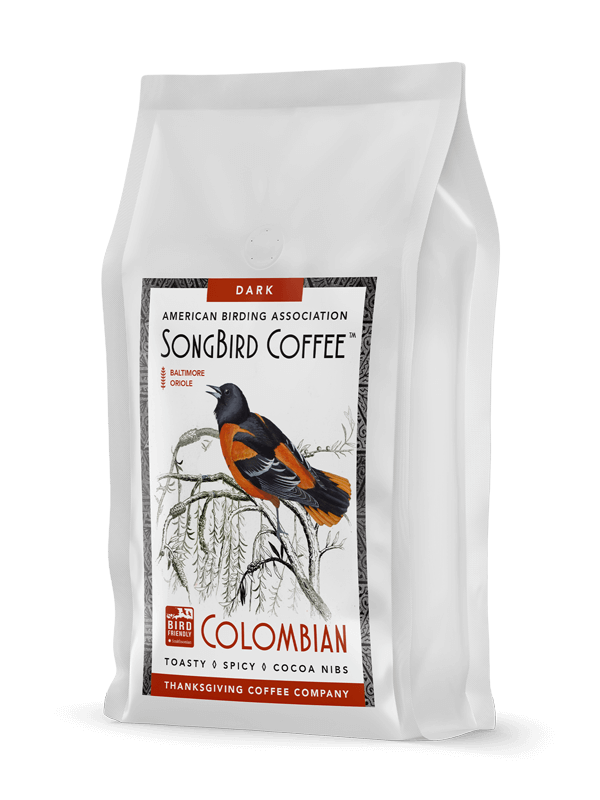 Dark roast SongBird Colombian coffee beans from Thanksgiving Coffee Company, showing roasted beans in a natural setting.