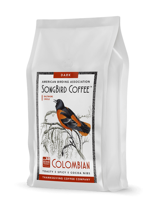 Dark roast SongBird Colombian coffee beans from Thanksgiving Coffee Company, showing roasted beans in a natural setting.